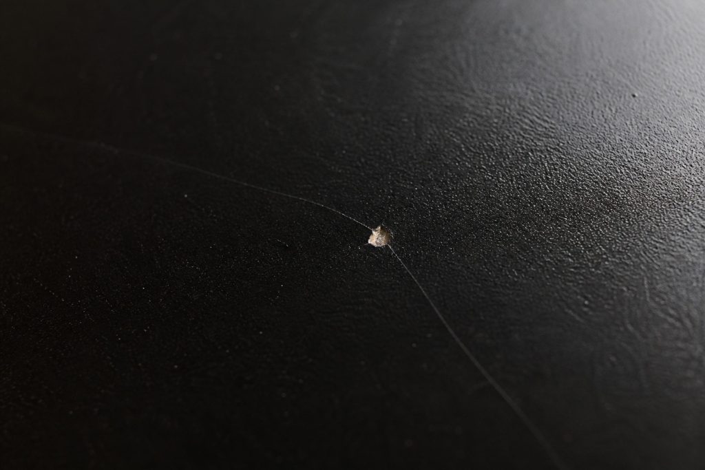 Black ceramic with a hairline crack running away from a small chip, raking light along the surface.
