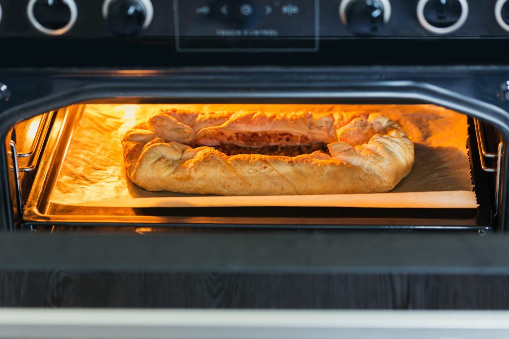 A built-in oven with the door open and a tart baking on the shelf, the cavity lit warm, knobs and a touch control panel above the door