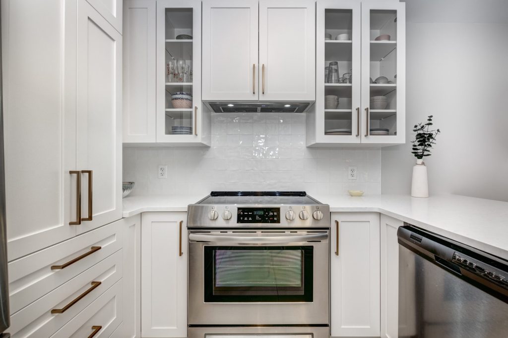 A stainless slide-in range set between white shaker cabinets under a hood, a dishwasher at the right, bright daylight