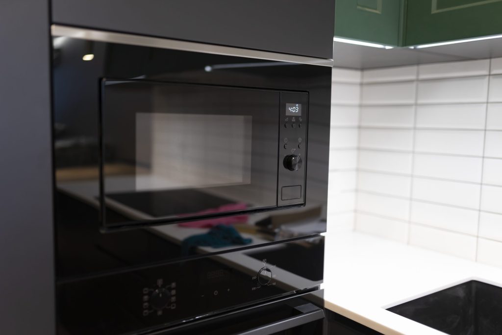 A black built-in microwave set into a run of dark cabinetry above a cooktop, its door closed