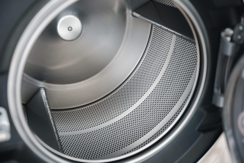 The inside of a dryer drum seen through the open door, the perforated stainless wall and the lifting vanes