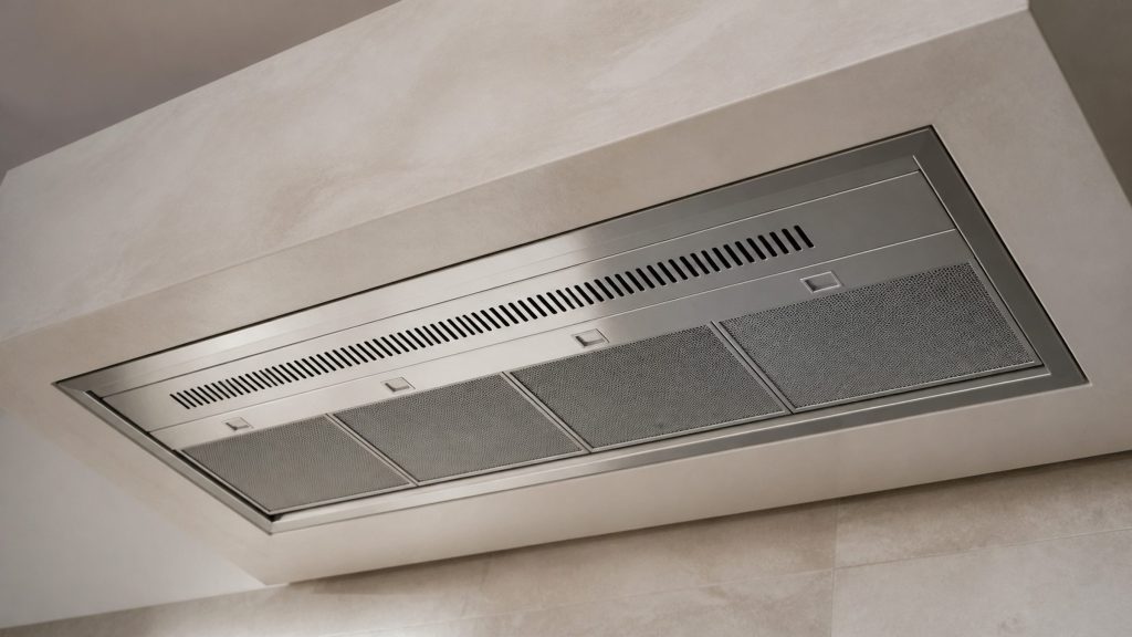 A custom hood liner set into the underside of a built plaster canopy, only the stainless insert and its filters visible from below.