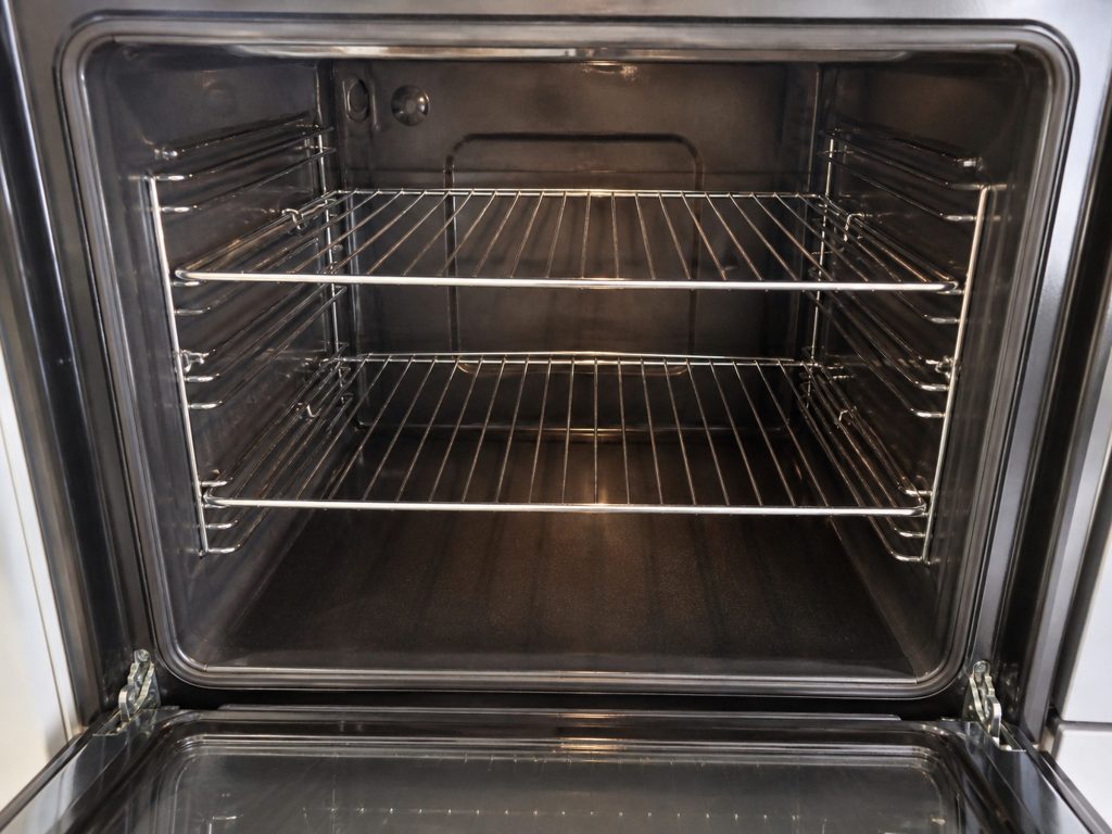The inside of a wall oven cavity with the door open, showing the side rack rails, two wire racks and the hidden bake element under the floor.