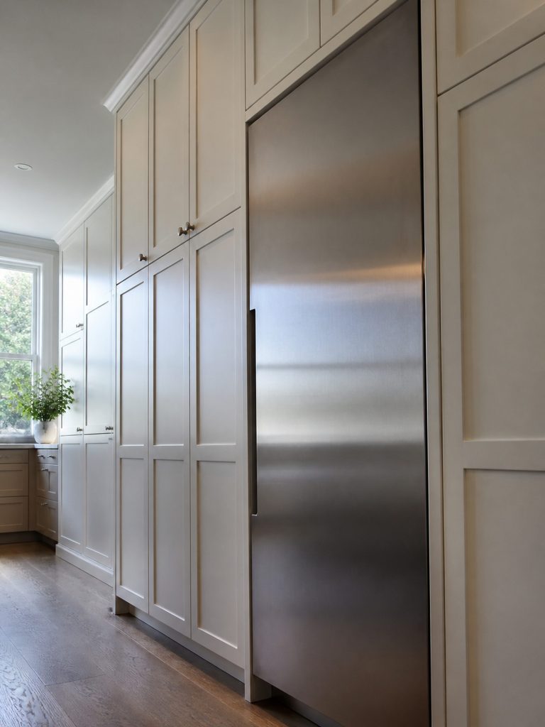 A tall run of pale kitchen cabinetry with a stainless appliance column built into it, seen from below at an angle so the cabinetry dominates and the appliance front is foreshortened.
