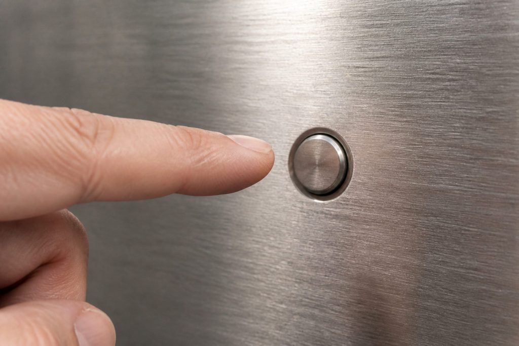 A single finger about to press a control on a brushed steel appliance fascia.