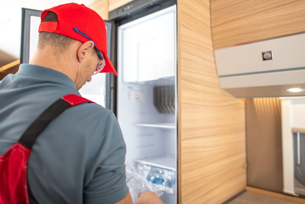 A repair technician looking into an open refrigerator in a fitted kitchen