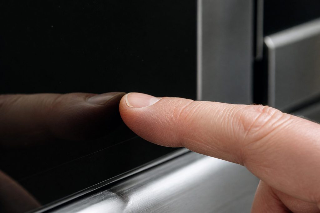 A fingertip on dark blank glass beside a closed appliance door, nothing lit beneath it.