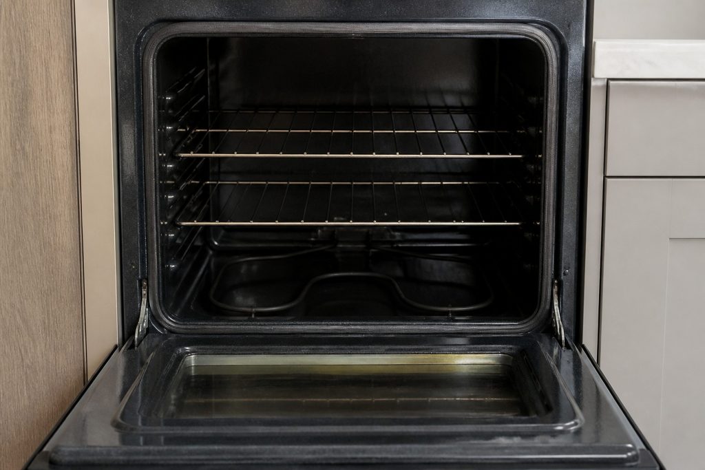 An empty oven cavity with the door open, the racks in place, the bake element at the bottom dark and cold.