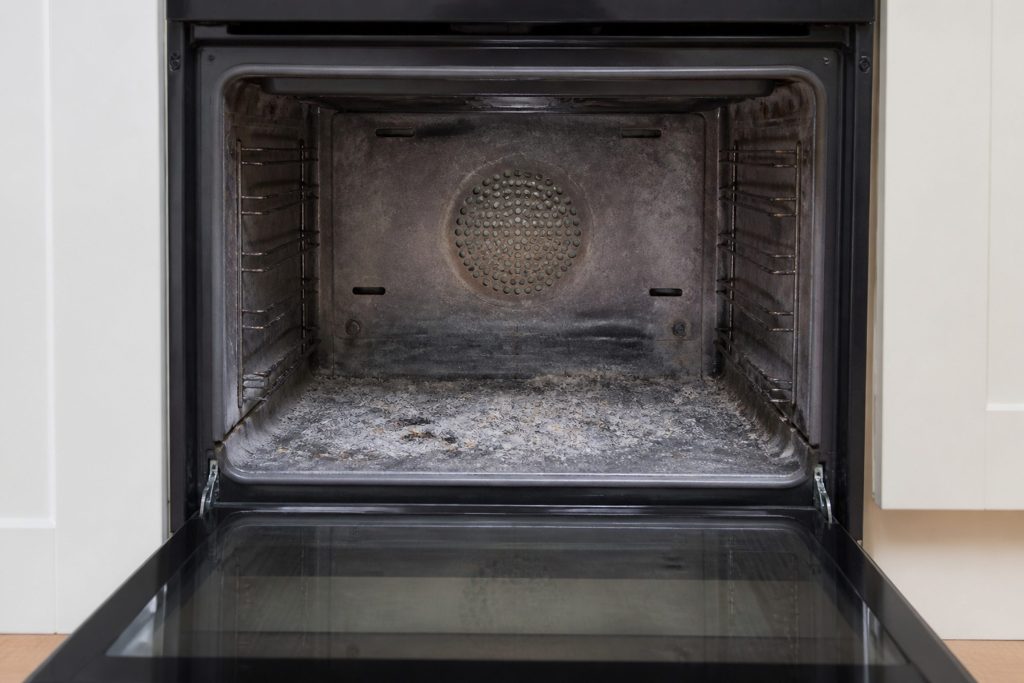 An oven cavity after a very hot cycle: white ash across the floor of it, the door open, the interior discolored.